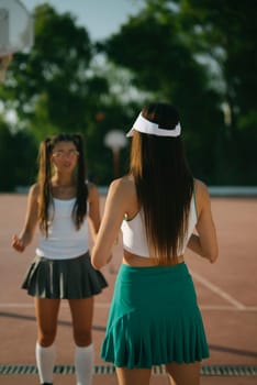 Two spirited young women enjoy a fun moment together on a sunny tennis court in their stylish sporty attire