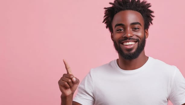 Young adult man is smiling and pointing up with his index finger against a pink background