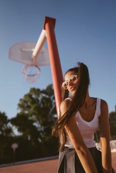 A vibrant young woman poses at a basketball court under the warm sun, showcasing her energetic style.