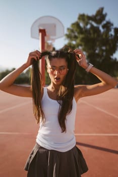 A cheerful girl is having fun enjoying a sunny day on the basketball court, showcasing her playful hairstyles