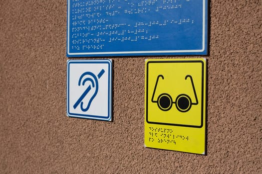 Blind and deaf person icon next to braille text for information for people with disabilities. Social amenities for disabled people, building wall with sign for handicapped people