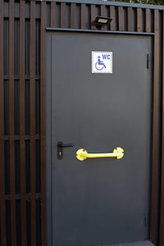 Entrance door to public toilet for disabled people, vertical photo of door with wheelchair sign at entrance to WC on street, accessible area for people with disabilities, outdoor toilet