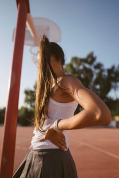 A young woman with long flowing hair strikes a pose on a basketball court as the sun sets beautifully in the background