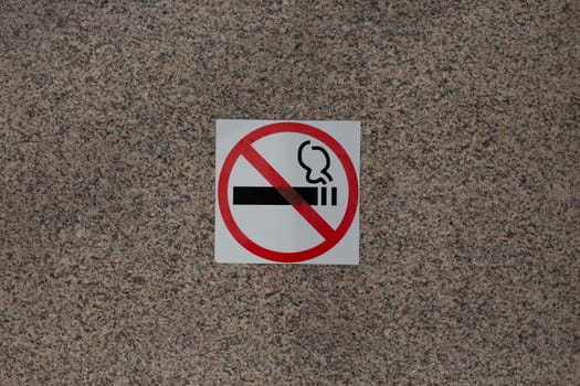 Sticker with crossed out cigarette on marble wall of building, ban on smoking in public place with special sign, social problem and smoking addiction