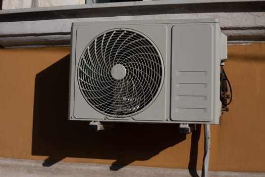 Photo of an air conditioner on wall of building, fan for taking air from the street and cooling house in hot weather, air conditioner on facade