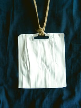 A wrinkled blank name tag hanging from a twine string, set against a dark blue fabric background.
