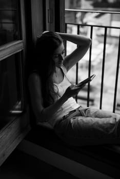 A serene moment of a woman enjoying her phone by the window, embodying relaxation and introspection.