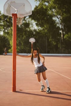 A girl dressed in a sporty outfit, enjoying a game of basketball on an outdoor court under the bright sunlight