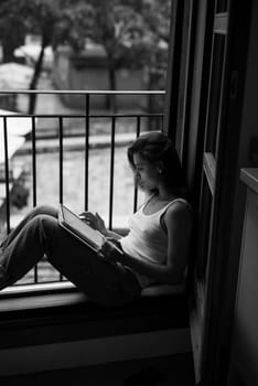 In a peaceful window setting, a woman immerses herself in a captivating book that embodies tranquility and leisure