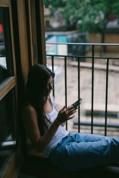 A tranquil and serene moment was beautifully captured showing a woman completely engrossed in her phone by a window