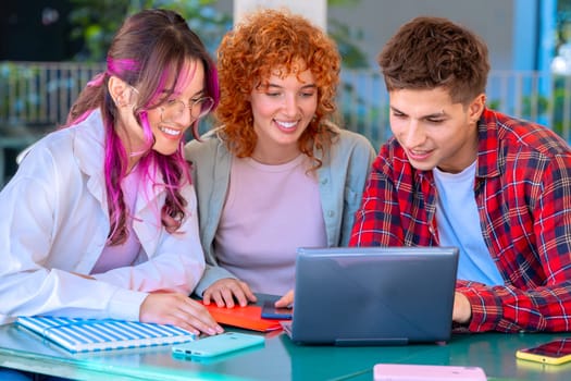 A group of three students with laptops and notes sit near the campus to review the exam.tudents with laptops sit near the campus and communicate. High quality photo