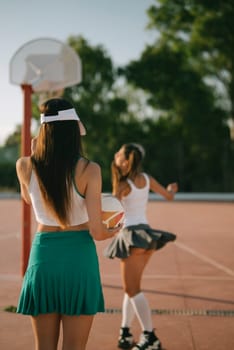 Two girls dressed in colorful sporty outfits are enjoying a fun and exciting game of basketball outdoors