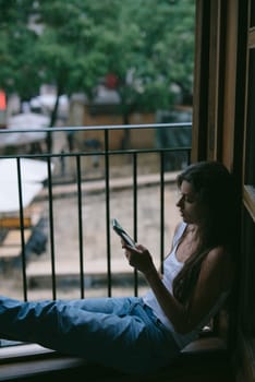 A peaceful and serene moment of a young woman deeply enjoying her phone while comfortably seated by the window