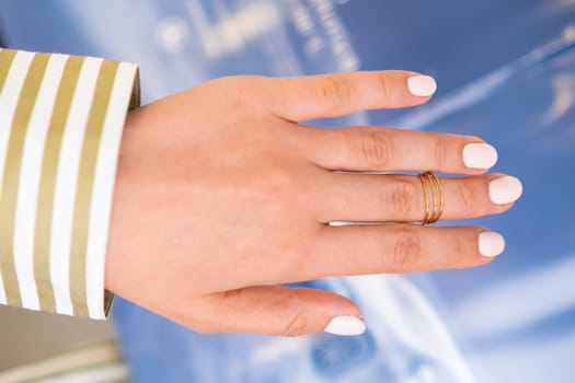 A stylish manicure featuring pale gel polish is showcased on a hand with a delicate ring.