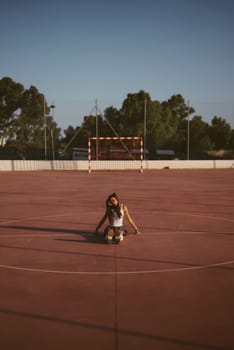 A tranquil scene of a young girl peacefully sitting alone on an empty basketball court during a beautiful sunset