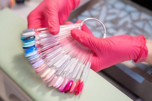 Nail master holding a collection of nails color polish samples. A palette of transparent tips with different colors.