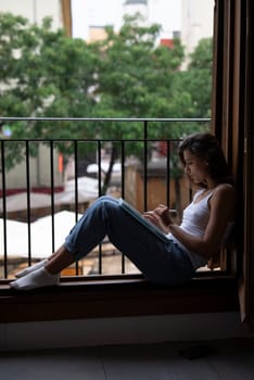 A woman finds enjoyment in a peaceful moment by her window, lost in deep thought and embraced by lush greenery