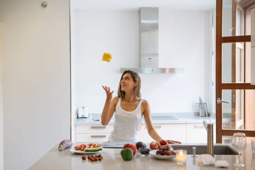 A playful woman skillfully juggling several pieces of cheese in a vibrant bright kitchen filled with fresh fruits