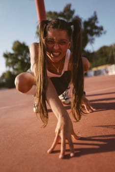 A determined and enthusiastic young girl prepares herself intensely to sprint on an outdoor athletic track