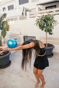 A joyful woman gracefully dances with a vibrant blue ball in a stylish, modern indoor environment, radiating energy