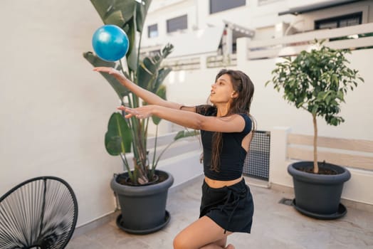 In an outdoor setting, a woman energetically performs a dynamic exercise routine using a blue exercise ball