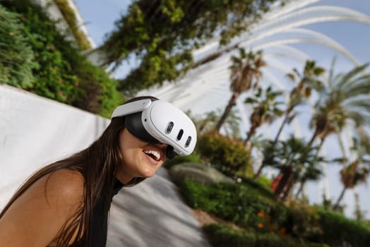A joyful young woman is fully immersed in cuttingedge virtual reality technology while surrounded by vibrant greenery