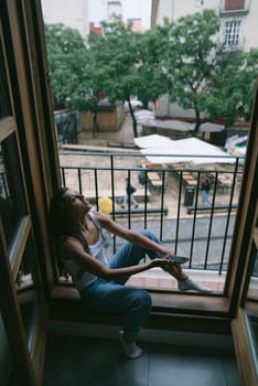 A woman sits by her window, lost in thought amidst the lush greenery and vibrant urban life around her