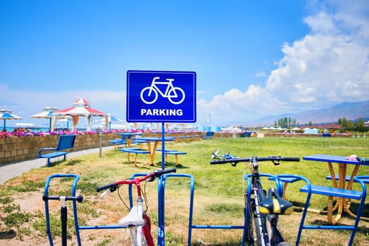 Bicycles are parked on a land lot next to a sign that says parking, as the blue sky and white clouds make a beautiful natural landscape