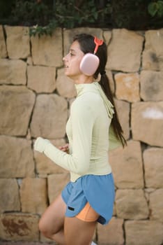 A young woman is happily enjoying a jog outdoors in a vibrant environment, wearing sporty attire and her headphones