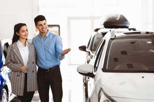 Visiting Car Dealership. Young family standing in auto showroom, looking for new vehicle