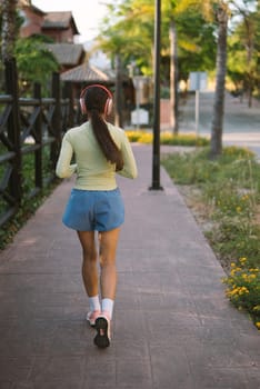 A young woman is jogging along a serene sidewalk in a tranquil park, fully enjoying the outdoor exercise experience