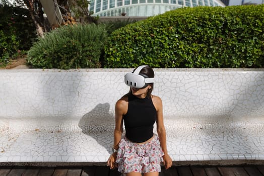 A young girl enjoys a captivating VR experience outdoors while wearing a headset in the sunny setting