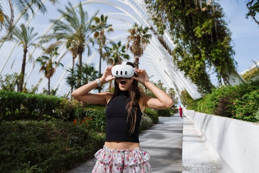 A cheerful young girl joyfully plays with her VR goggles while being surrounded by lush tropical greenery
