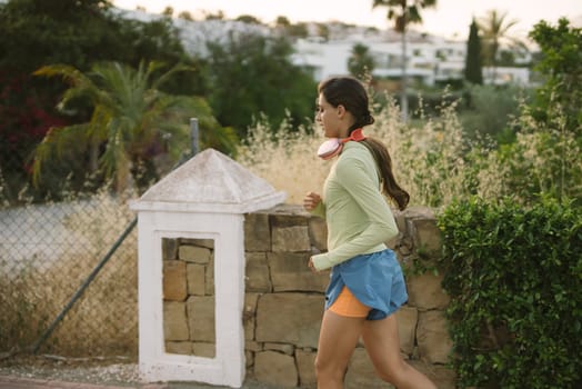 A woman jogs gracefully along a scenic and picturesque route that is surrounded by lush greenery and tall palm trees