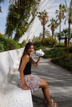 A woman sits in a beautiful park, enjoying a refreshing drink amid lush greenery and palm trees on a lovely day