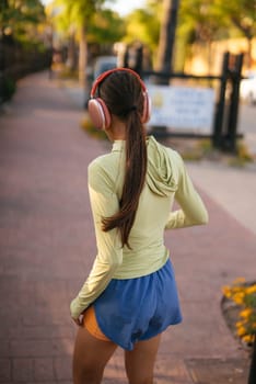 A young woman is enjoying her time jogging outdoors while wearing her favorite headphones in a vibrant urban setting