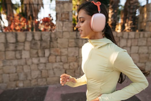 A woman jogs in a fashionable outfit while enjoying music through cozy ear muffs in an inviting outdoor setting