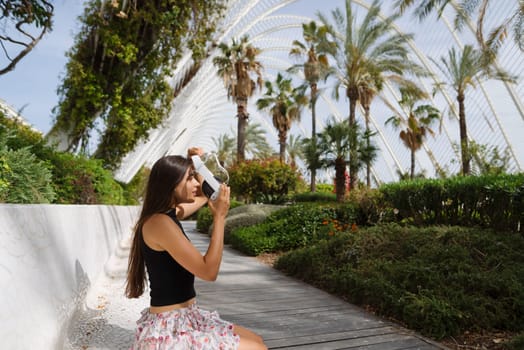 A young woman captures memories in a lush garden filled with palm trees and vibrant greenery around her