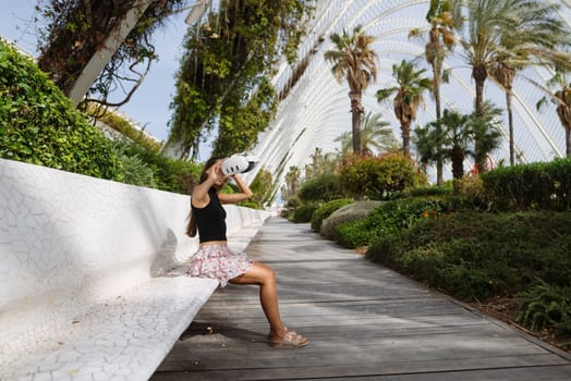 A stylish woman relaxes on a bench in a modern park filled with lush palm trees, creating a picturesque scene