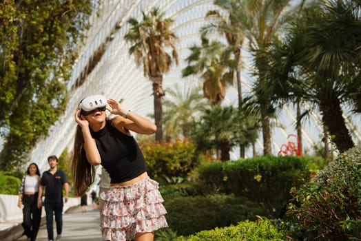 A stylish and playful young woman strikes a pose in a vibrant garden setting that showcases beautiful palm trees