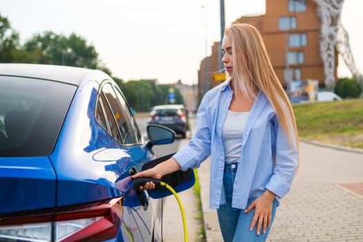 Blonde woman with long hair connects her electric car to a charger at a street side station