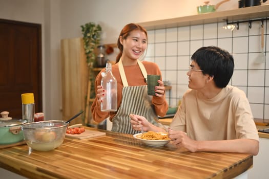 Happy young couple chatting and enjoying their lunch in domestic kitchen.