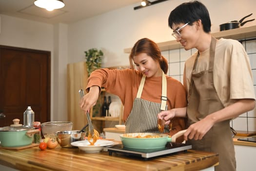 Happy young couple cooking pasta together in the kitchen. Relationships and happy domestic life.