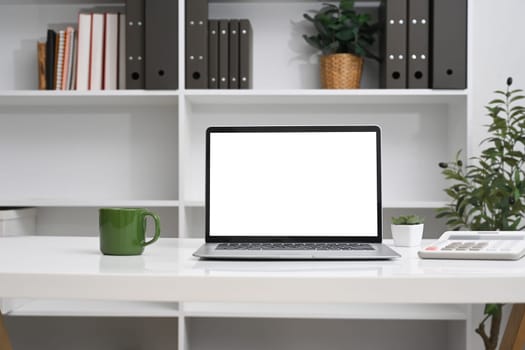 Front view laptop with empty screen, coffee cup and calculator on white table.