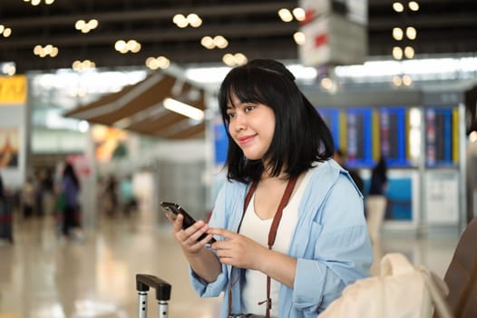 Happy young female traveler using mobile phone at airport waiting the flight.