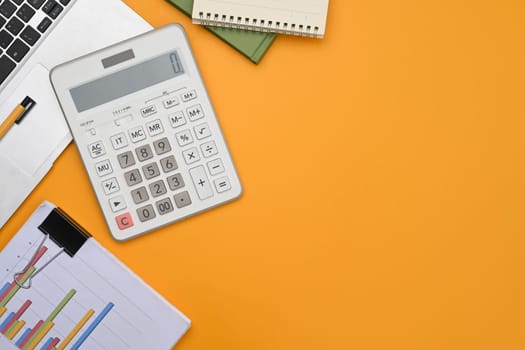 A calculator, laptop, financial reports and notepad on yellow background with space.