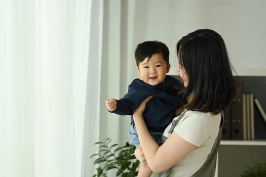 Loving asian mother holding her smiling baby in her arms. Family, love and childcare concept.