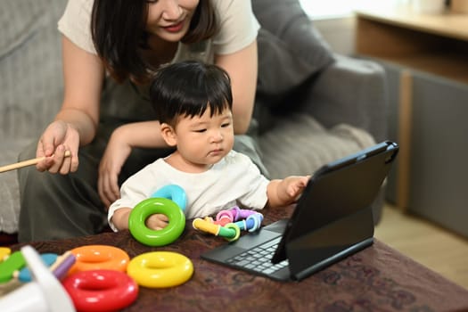 Cute little boy with mom sitting in living room looking at digital tablet screen.