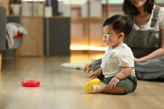 Little toddler boy playing with toys on wooden floor at home. Child development and learning concept.