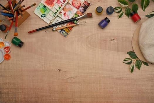 Variety of art supplies including paint brushes, watercolor paint and palette on wooden background.
